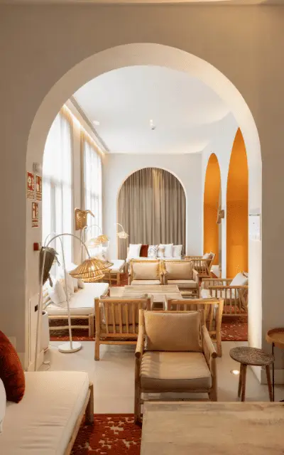http://A%20cozy,%20inviting%20lounge%20with%20soft%20beige%20chairs%20and%20sofas,%20warm%20lighting,%20and%20arched%20doorways.%20The%20atmosphere%20is%20serene%20and%20elegant,%20exuding%20warmth.