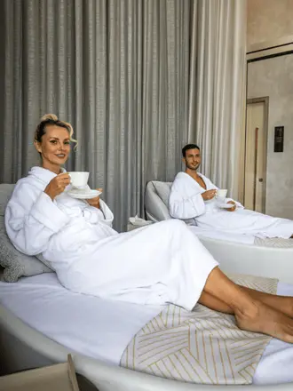 http://A%20man%20and%20woman%20in%20white%20robes%20relax%20on%20lounge%20chairs,%20sipping%20tea%20in%20a%20serene%20spa%20setting%20with%20neutral%20tones%20and%20soft%20lighting.