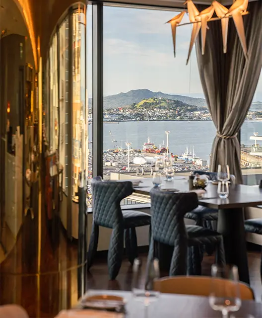 http://A%20four%20person%20restaurant%20table%20next%20to%20a%20large%20window%20looking%20over%20a%20large%20port%20with%20mountains%20in%20the%20background