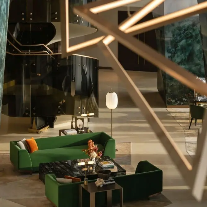 Modern hotel lobby with elegant decor. Features green sofas, a black spiral staircase, geometric chandelier, and warm lighting, creating a luxurious ambiance.