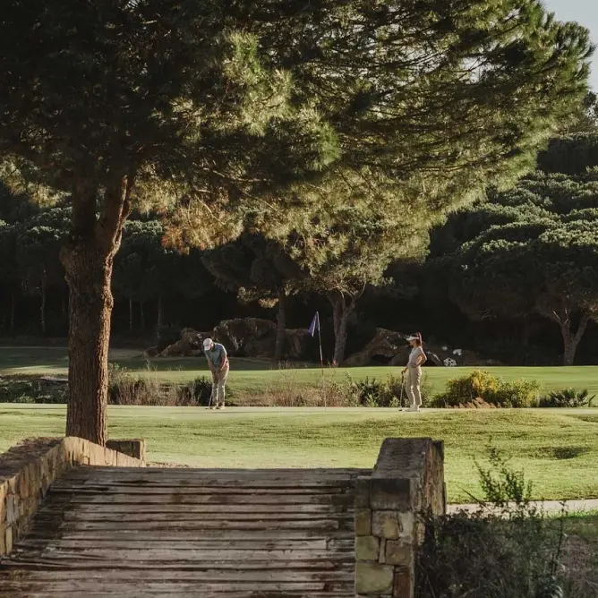 A man walking along a grassy path on a golf course, surrounded by trees and open space.
