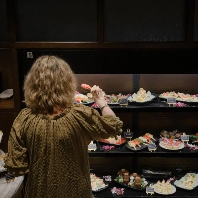 A woman seen from behind choosing a sweet treat from a multi-tiered dessert buffet display.