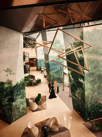 http://Modern%20hotel%20lobby%20with%20abstract,%20geometric%20sculptures%20hanging%20from%20a%20high%20ceiling.%20Large%20murals%20depict%20lush%20green%20landscapes,%20creating%20a%20serene%20atmosphere.