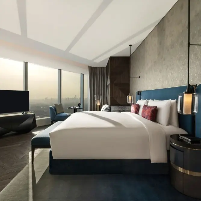 Stylish room with cozy gray chaise, gold pillows, and a marble side table with an open book. Large windows reveal a serene sunset cityscape.