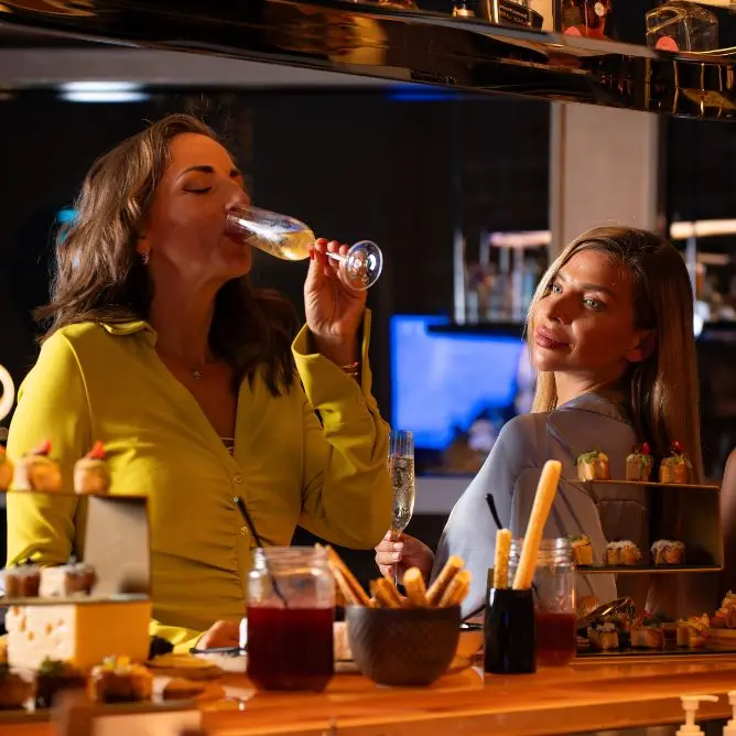 Women enjoying champagne and appetizers at a modern hotel bar counter.