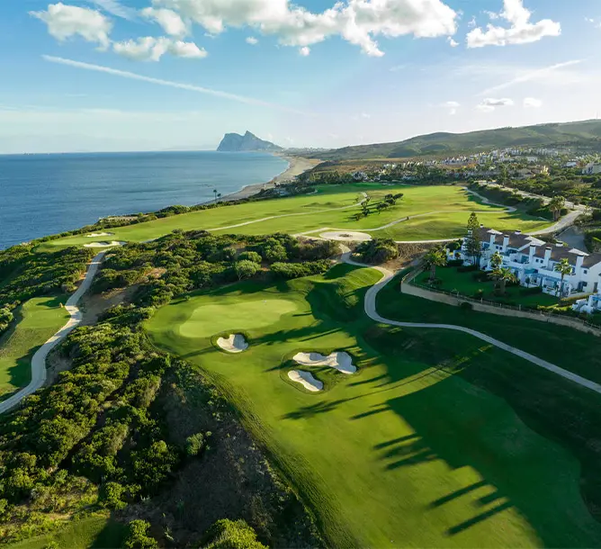 A birds eye view of a large fresh green golf course next to the sea