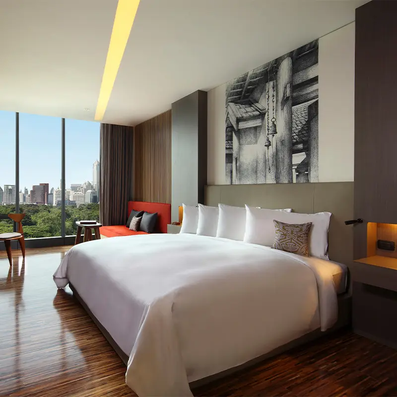 A large wooden-themed hotel room with a double bed. Daylight floods the room from the floor to ceiling windows.