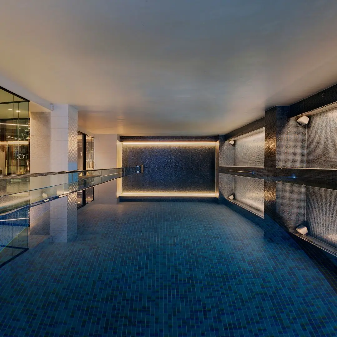 A luxurious interior view featuring a sleek swimming pool with a stunning skyline reflecting in the water at dusk.