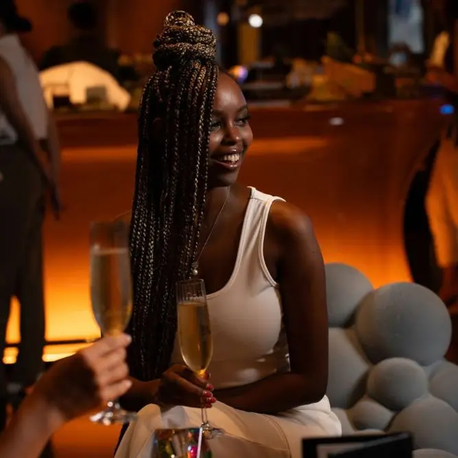 Smiling woman holding a glass of champagne in a warmly lit hotel lounge.